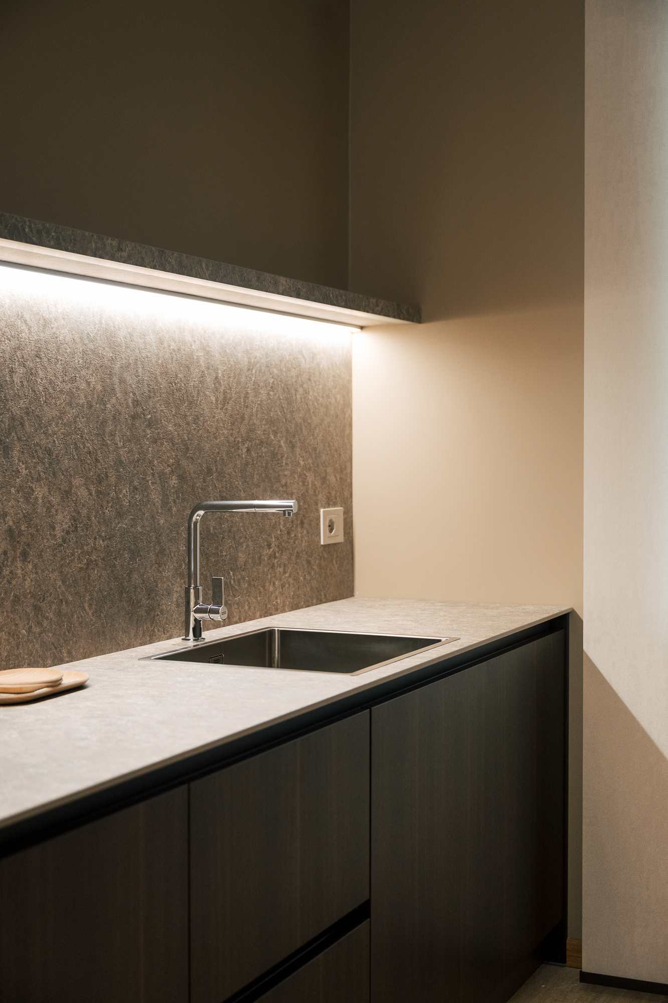 Dettaglio della cucina dell’ufficio con lavabo integrato, piano in pietra e illuminazione sottopensile