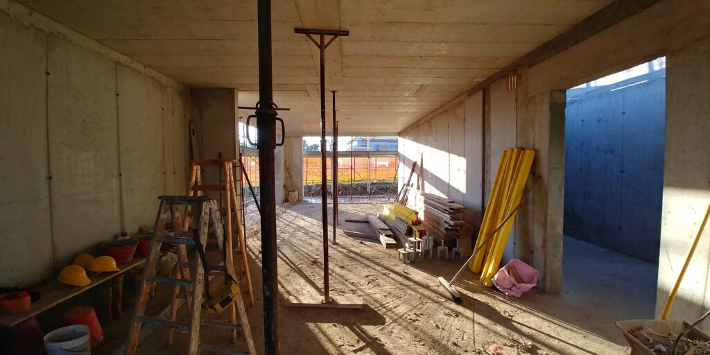 Interno della casa durante il cantiere con struttura in calcestruzzo e grandi aperture verso l’esterno