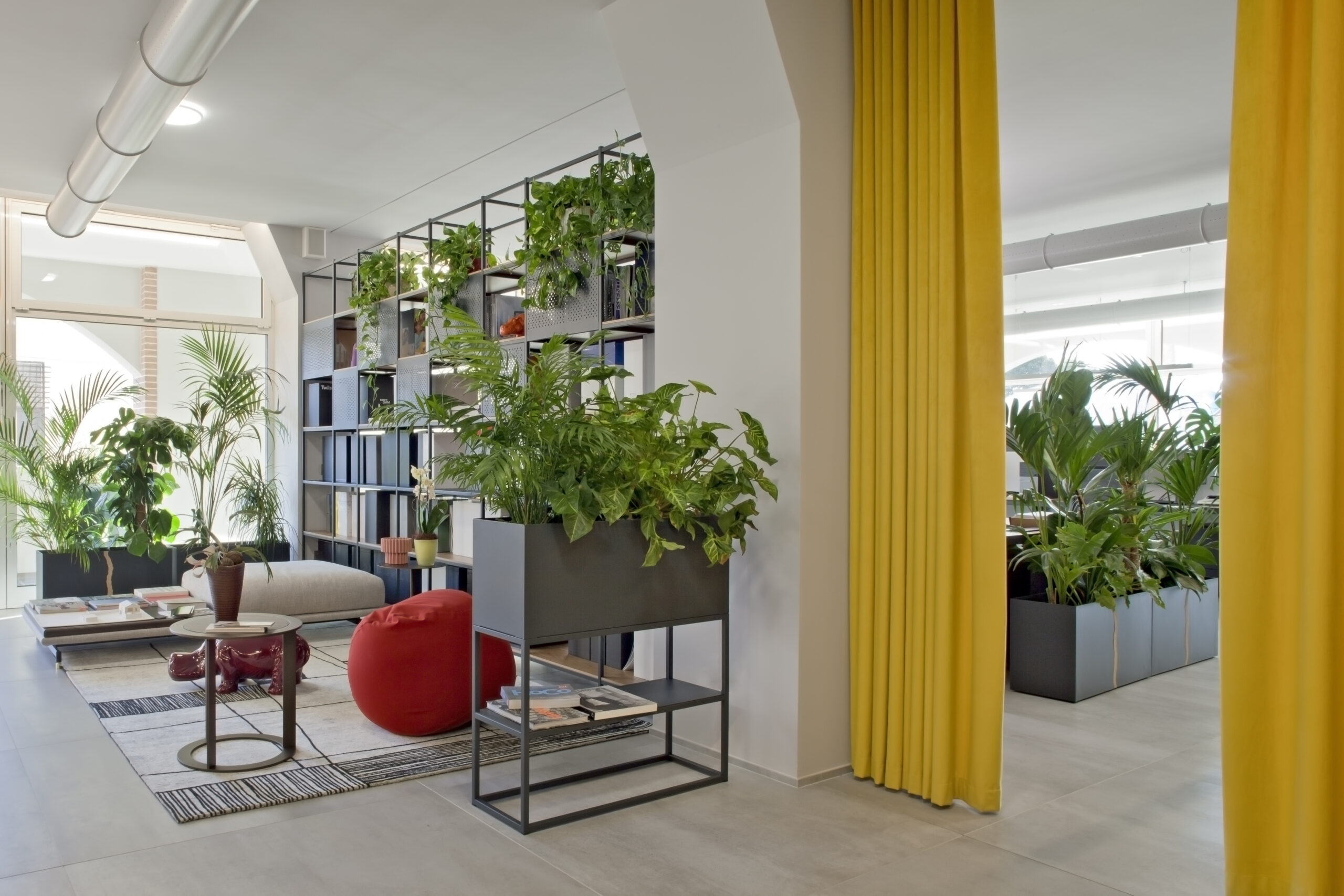 Area lounge dell’ufficio con arredi domestici, piante e tende gialle