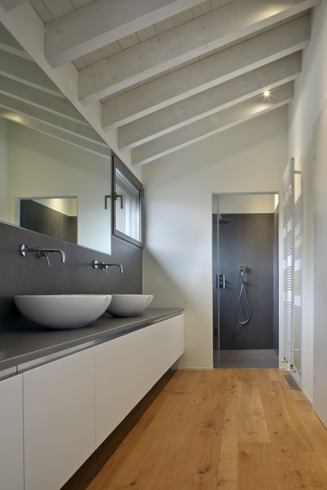 Casa GZ, bagno con pavimento in legno, doppio lavabo e soffitto a falda