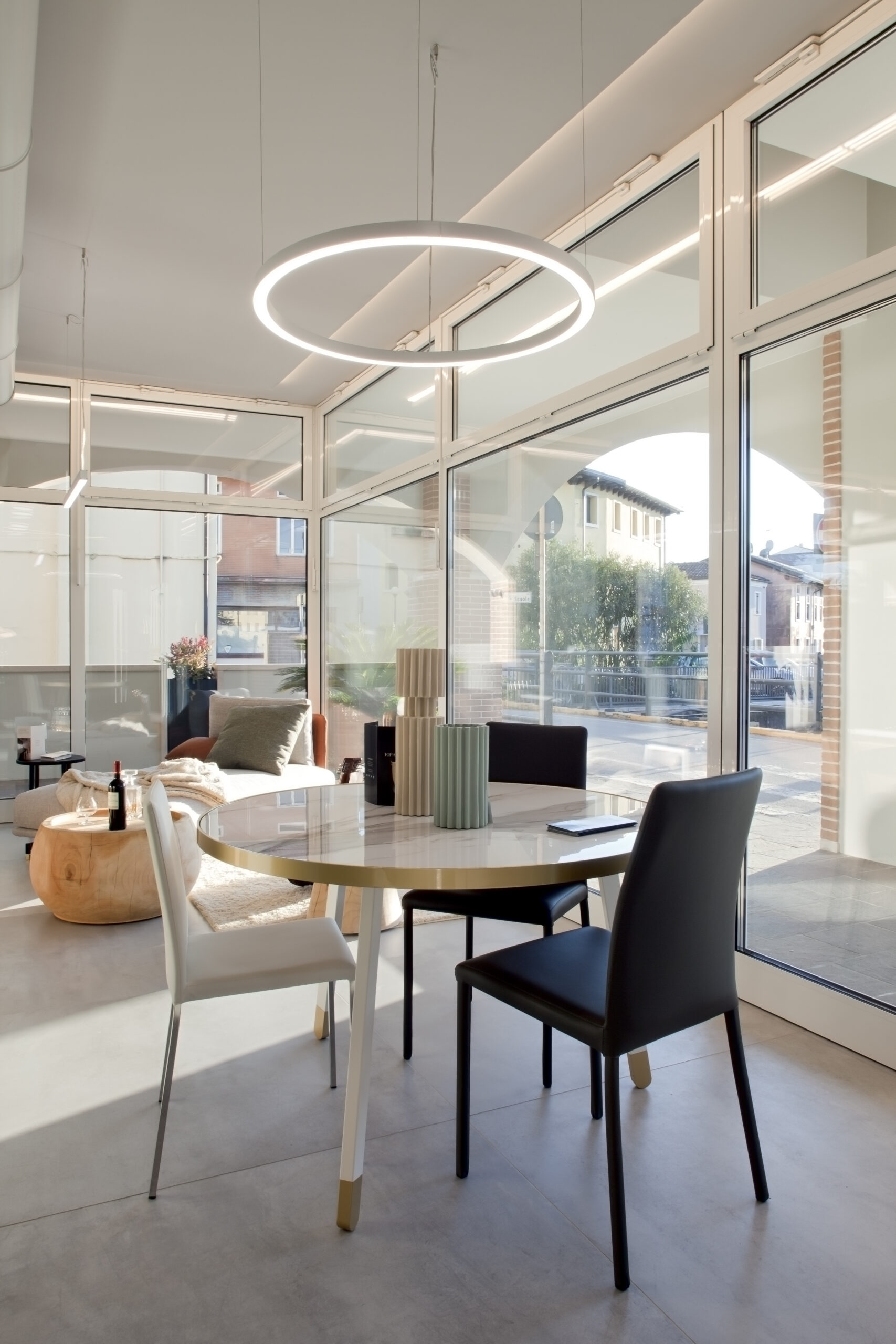 Area riunioni luminosa con tavolo rotondo, grandi vetrate e lampada sospesa