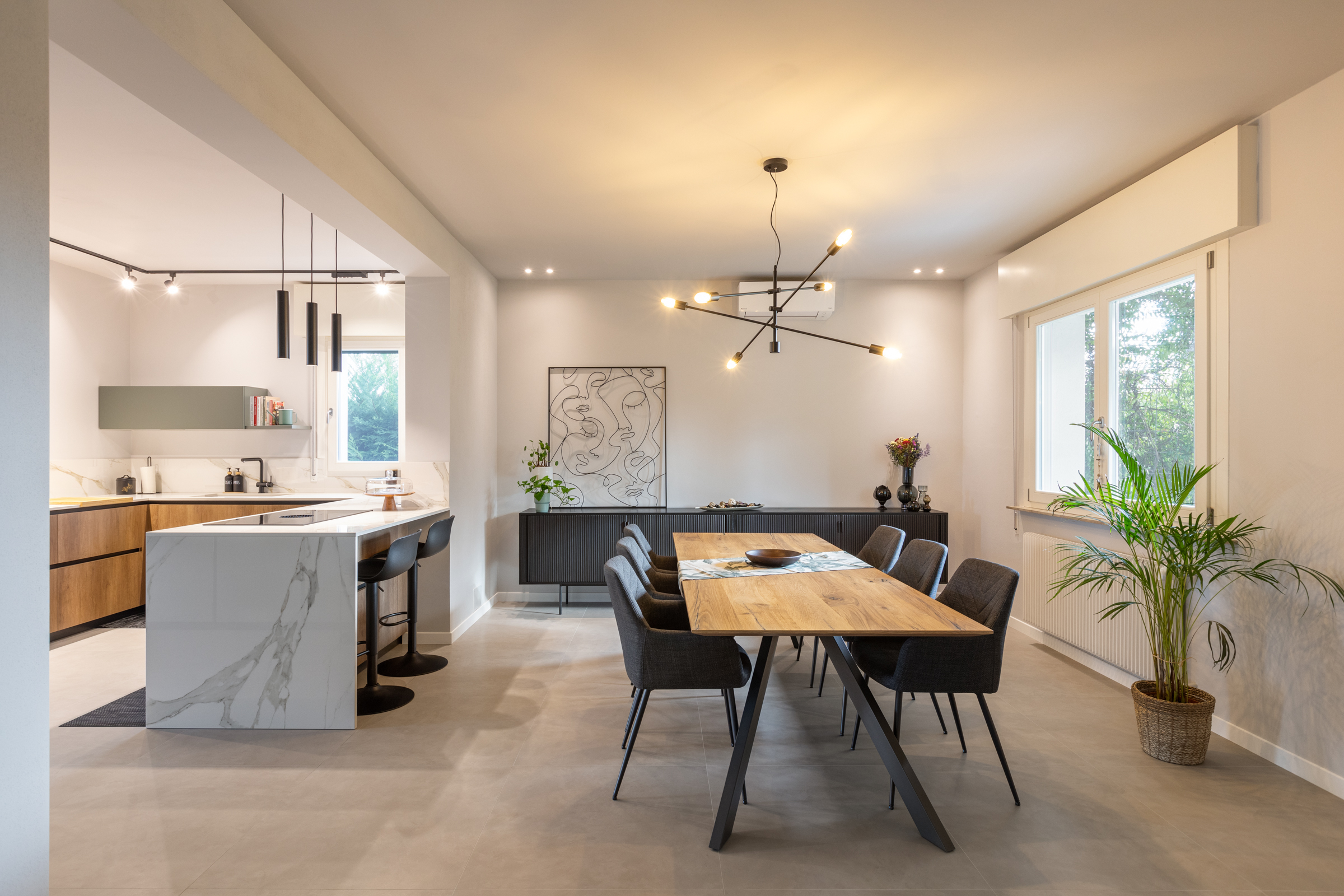 Zona giorno ristrutturata in casa anni Sessanta con cucina aperta e tavolo in legno