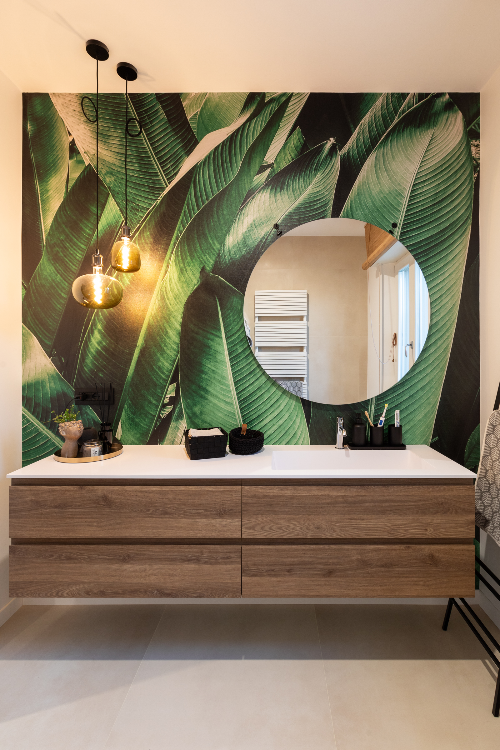 Bagno con parete botanica, specchio rotondo e mobile lavabo in legno