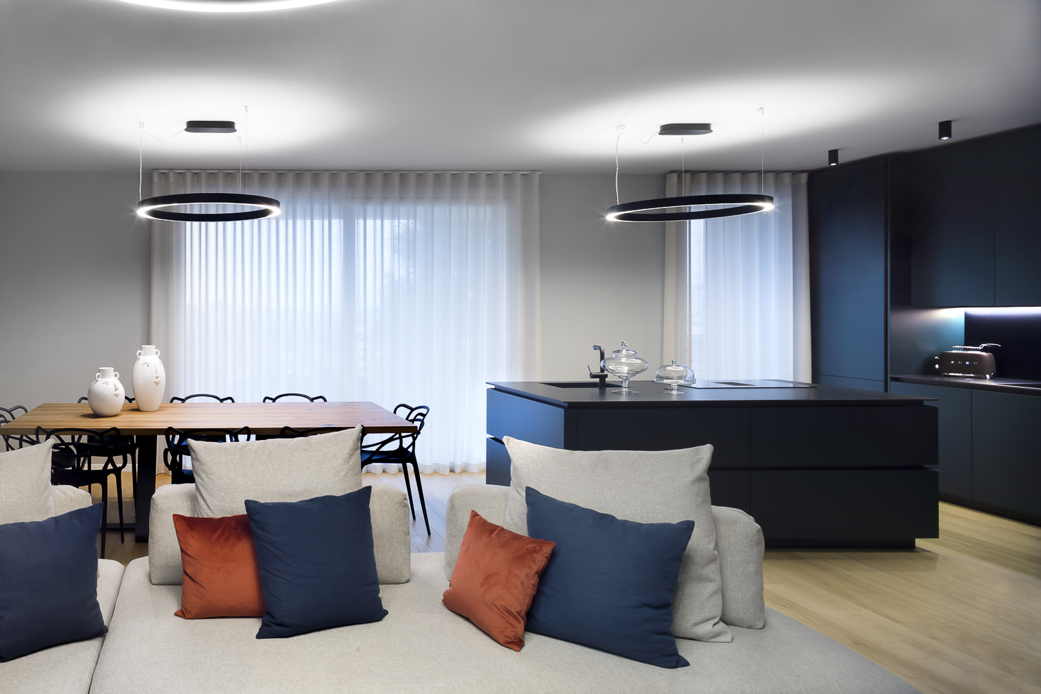 Appartamento GM, cucina con isola centrale e grande tavolo in legno, divano con cuscini colorati