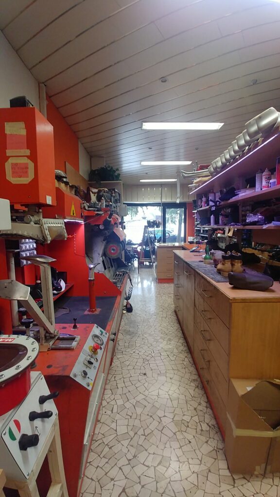 Calzoleria prima del rinnovo con macchinari a vista, scaffalature e spazio operativo poco ordinato