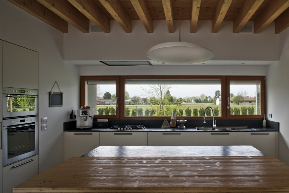 Casa CP, cucina con travi in legno e lunga finestra sul paesaggio