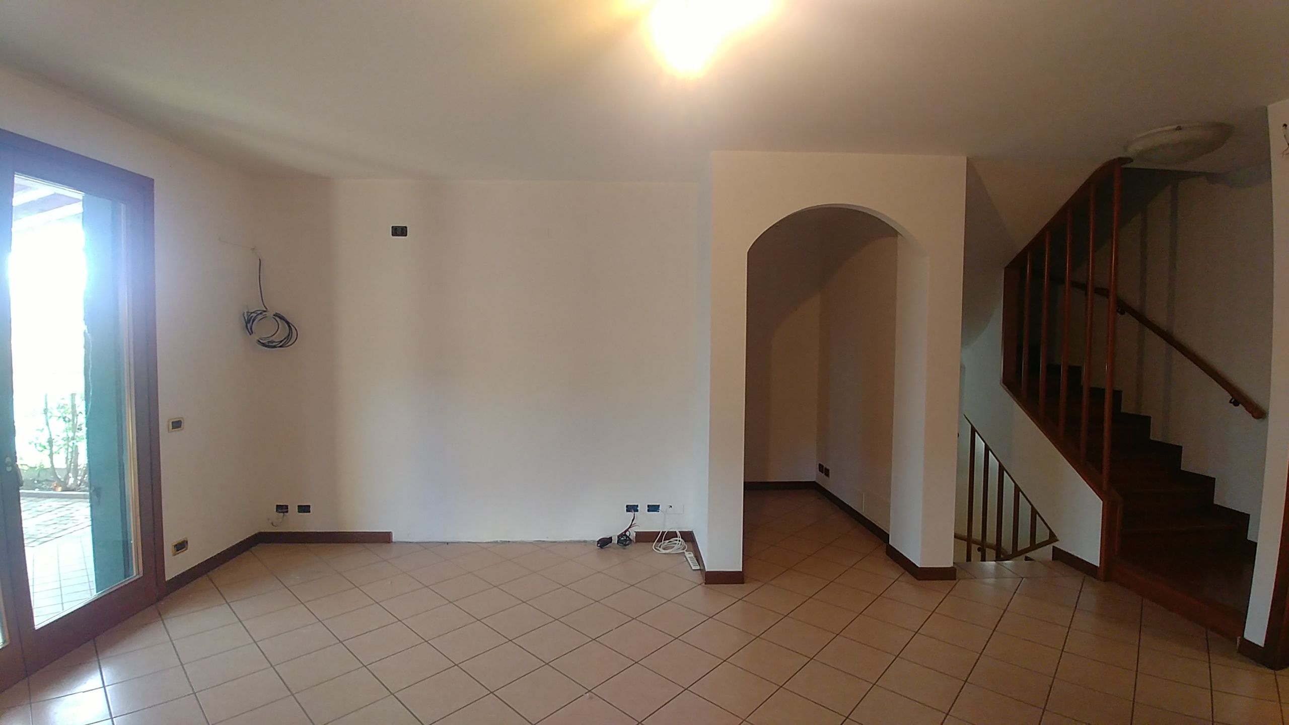 Soggiorno prima della ristrutturazione con distribuzione chiusa, finiture esistenti e scala a vista