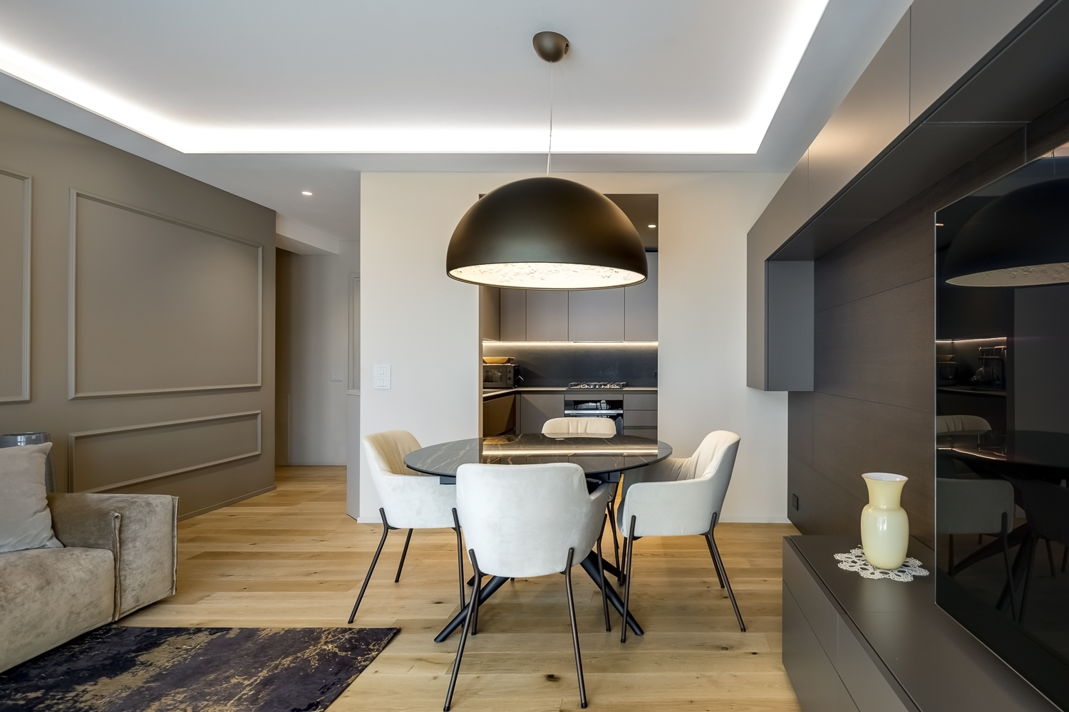 Appartamento C, zona pranzo con tavolo nero, lampada sospesa e parete attrezzata in legno scuro