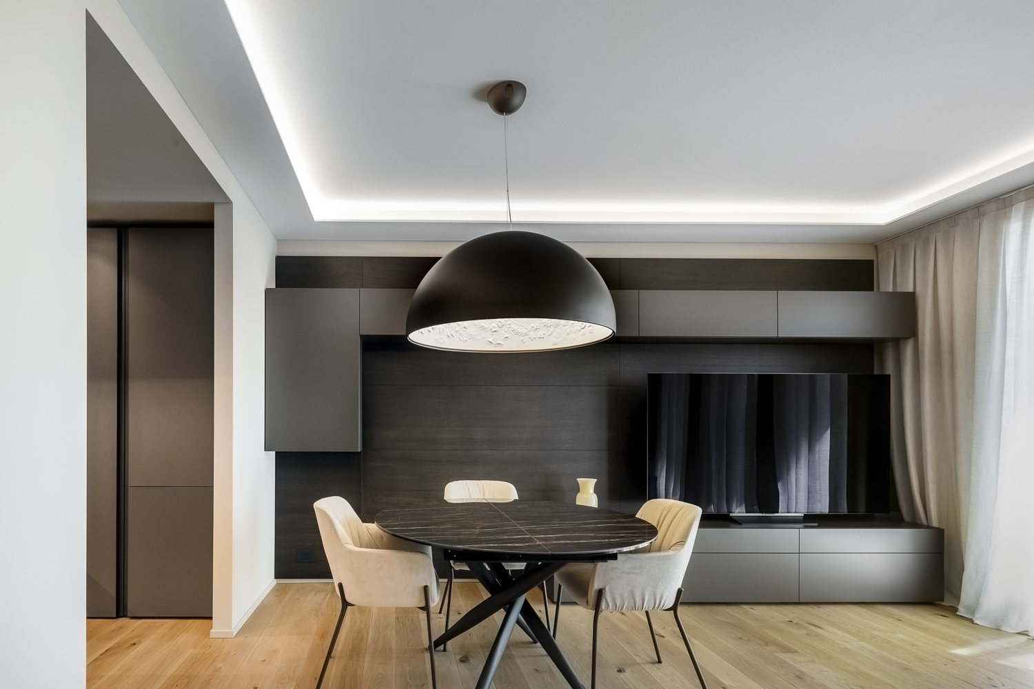 Appartamento C, zona pranzo con grande lampada sospesa, parete attrezzata in legno scuro e luce indiretta a soffitto