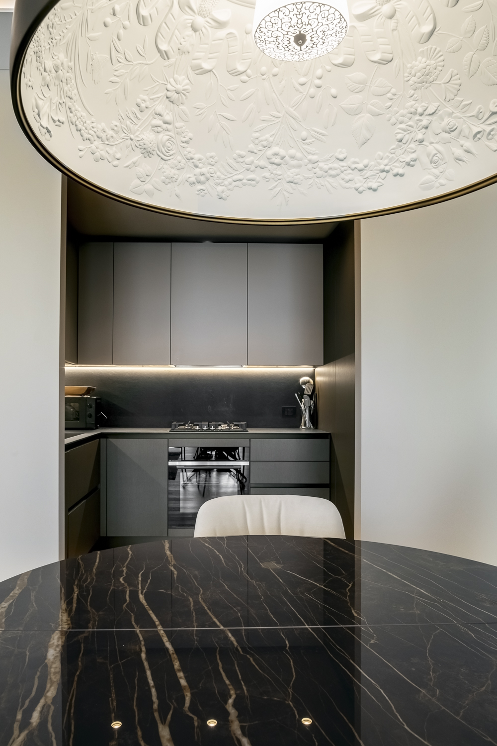 Appartamento C, zona pranzo con tavolo nero effetto marmo Noir Désir, lampada sospesa decorativa e cucina sullo sfondo