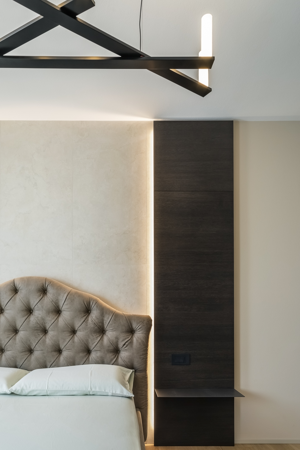 Appartamento C, camera da letto con testiera imbottita, pannello in legno scuro e illuminazione indiretta