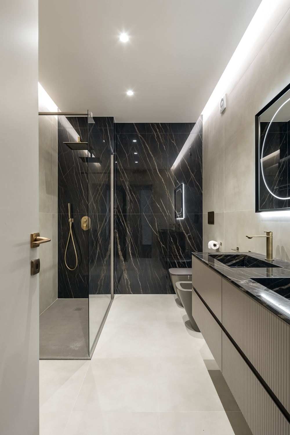 Appartamento C, bagno con doccia rivestita in effetto marmo Noir Désir, mobile lavabo sospeso e illuminazione indiretta