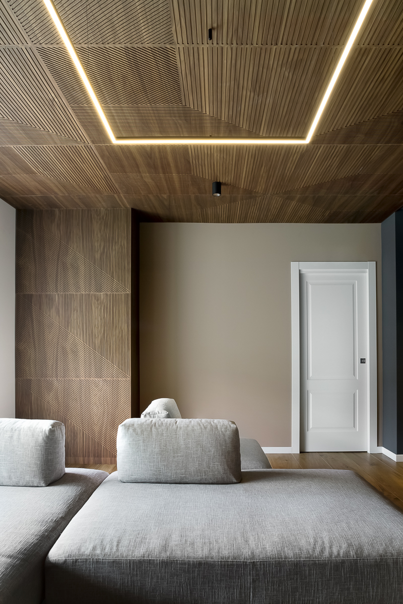 Appartamento YL, soggiorno con divano grigio, rivestimento in noce canaletto e illuminazione integrata a soffitto