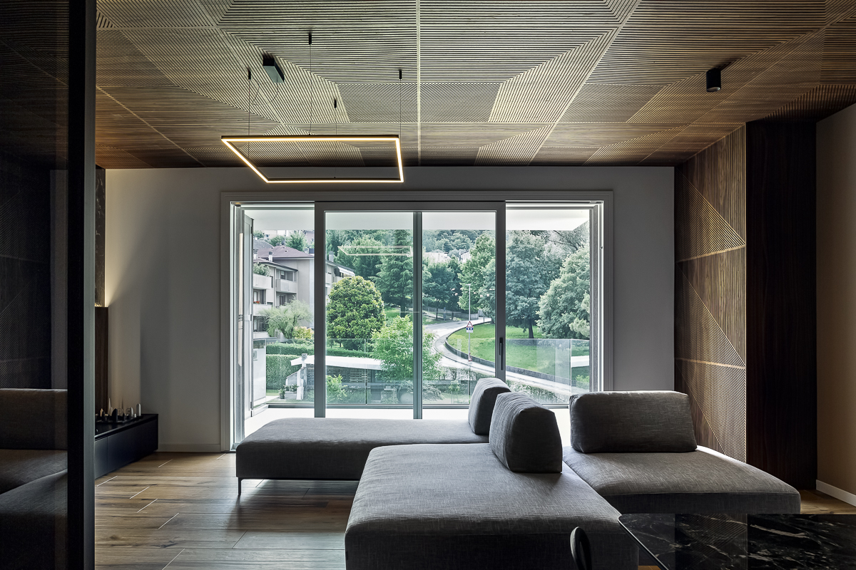 Appartamento YL, soggiorno con divano grigio, grande vetrata sul verde e soffitto rivestito in noce canaletto