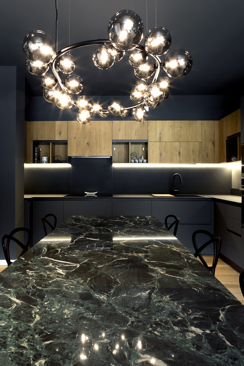 Appartamento YL, zona pranzo con tavolo in marmo verde, lampada decorativa e cucina sullo sfondo