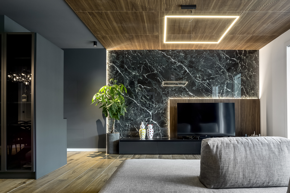 Appartamento YL, soggiorno con parete in gres effetto marmo Verde Alpi, soffitto rivestito in noce canaletto e divano grigio
