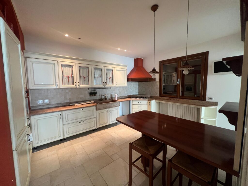 Cucina prima del restyling con arredi classici, finiture esistenti e pavimento in pietra color sabbia
