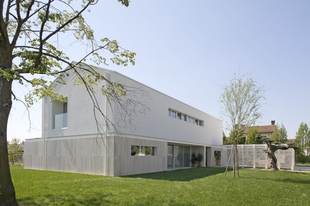 Casa P, vista esterna della villa contemporanea con basamento in travertino e facciata bianca