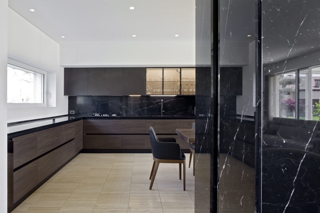 Casa P, cucina contemporanea con arredi in legno, superfici scure e continuità visiva con la zona giorno