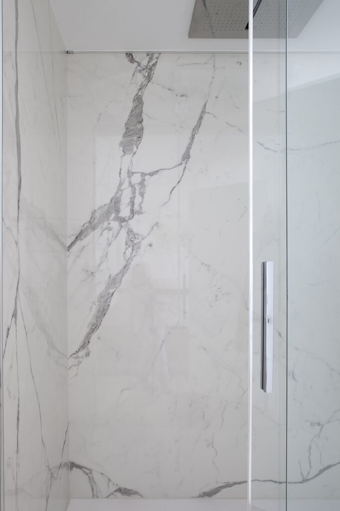 Casa P, dettaglio del bagno con rivestimento in marmo chiaro e box doccia in vetro